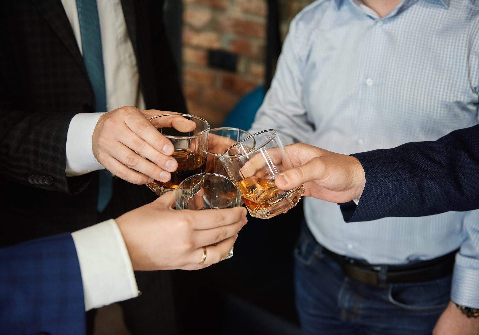 Group of four friends men in the whisky drink party holding glass of alcoholic beverages in their hands and clinking. Close up